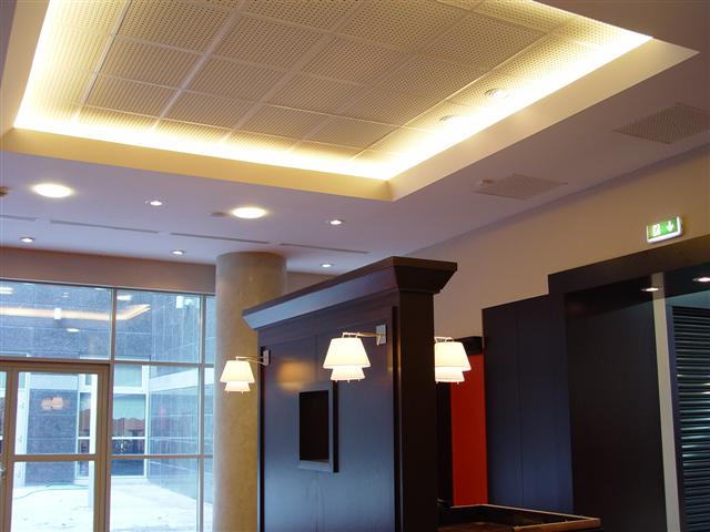 Perforowany sufit podwieszany z oświetleniem LED, widoczne ścianki działowe i filar w nowoczesnym biurze.